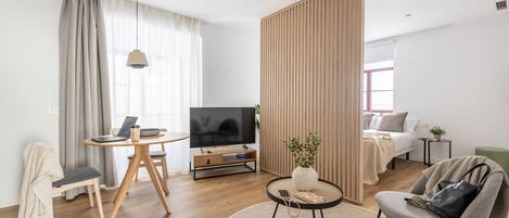 A modern living room with a TV, a laptop on a wooden table, a sofa, and a green armchair.