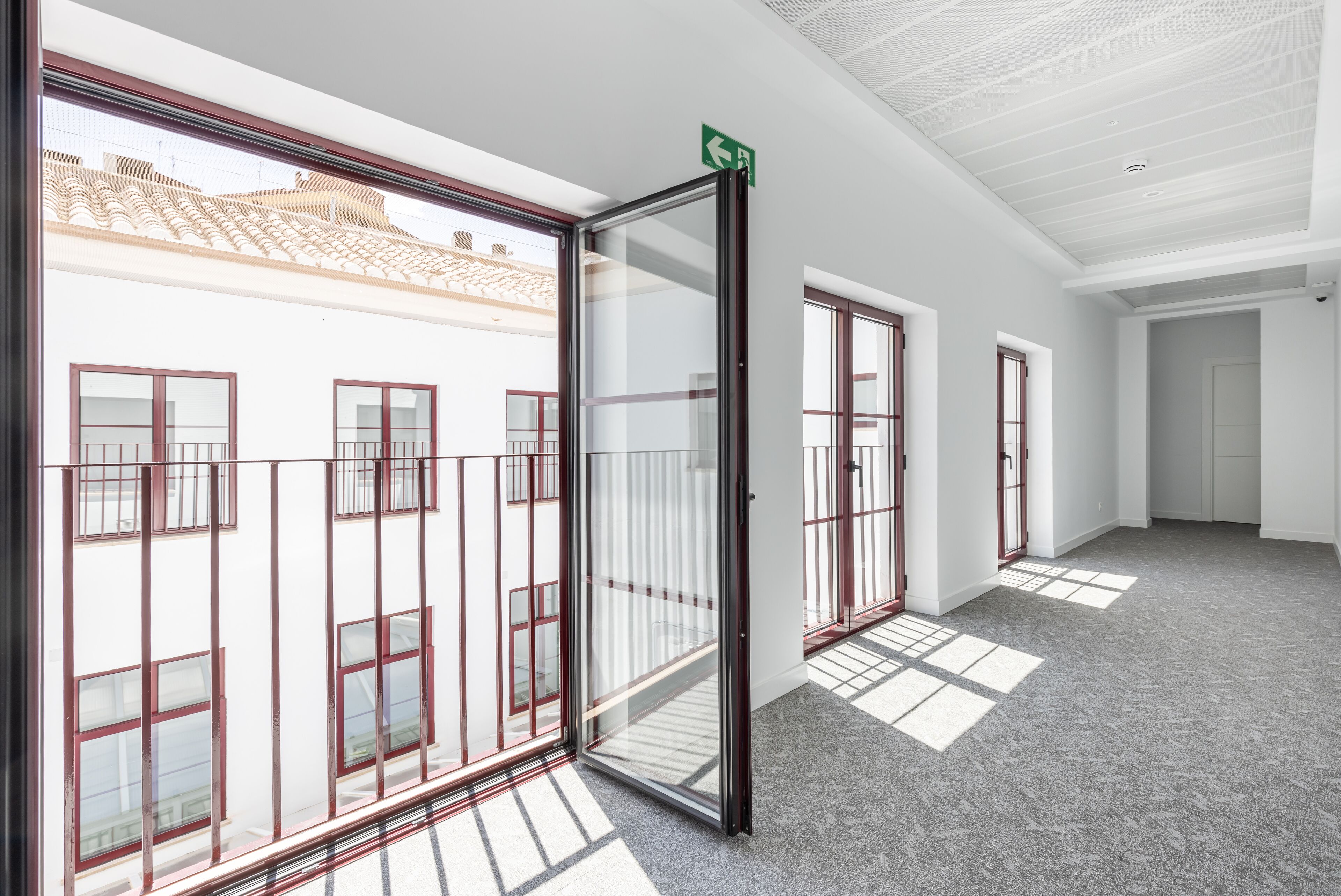 A corridor with large windows, a glass door, and a ceiling with recessed lighting.