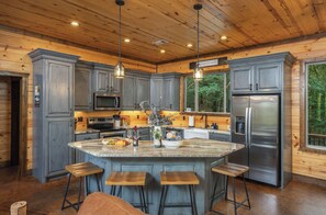 Une cuisine moderne dotée d ’un îlot central, de tabourets de bar, d’appareils électroménagers en acier inoxydable et de meubles de rangement en bois.