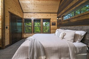 Un dormitorio de cabaña de madera con una cama grande, una ventana y una puerta.