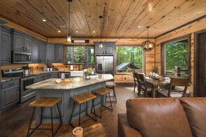 Una cocina amplia con una isla grande, armarios de madera y vistas al bosque circundante.