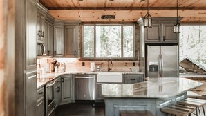 Eine moderne Küche mit Holzbalkendecke, Edelstahlgeräten und einer großen Kücheninsel mit Barhocker.
