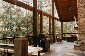 An outdoor deck with a grill, seating area, and a stone fireplace. - Majestic Cabin Escape - 4 Bdr I Hot Tub I Fire Pit I Slide I Lake close by (Broken Bow)