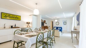 A dining area with a table set for four, a kitchen in the background, and a living area with a blue sofa. - Stunning villa with infinity pool, only 5 minute walk from the beach (Torre Delle Stelle (Maracalagonis))