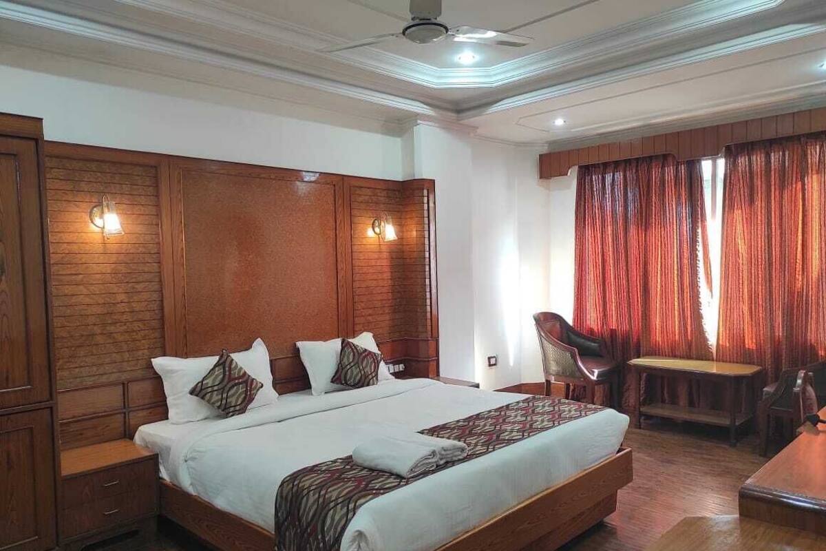 Quarto espaçoso com uma cama grande, cabeceira de madeira e uma escrivaninha com cadeira.