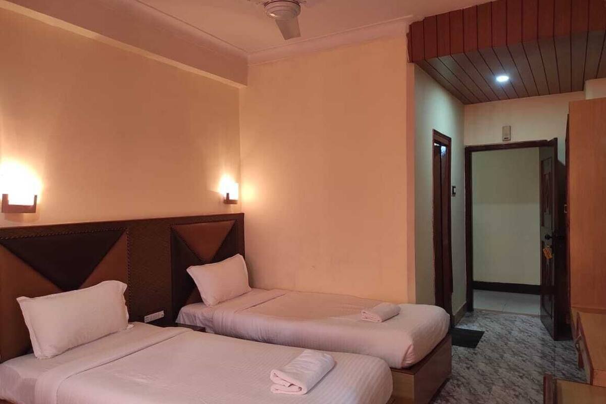 Quarto de hotel com duas camas, um ventilador de teto e uma porta que dá para outro cômodo.