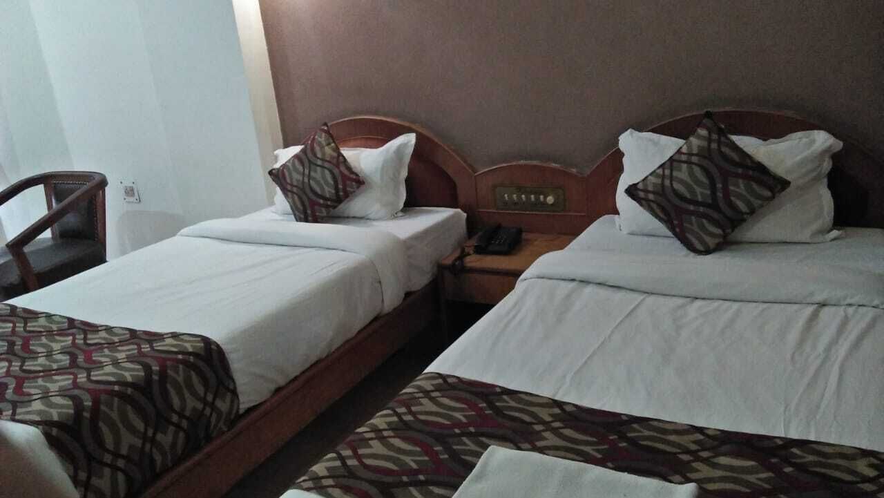 Ein Hotelzimmer mit zwei Einzelbetten, beide mit gemusterten Bettdecken und Kissen. Ein Nachttisch aus Holz beherbergt ein Telefon und eine Wanduhr.