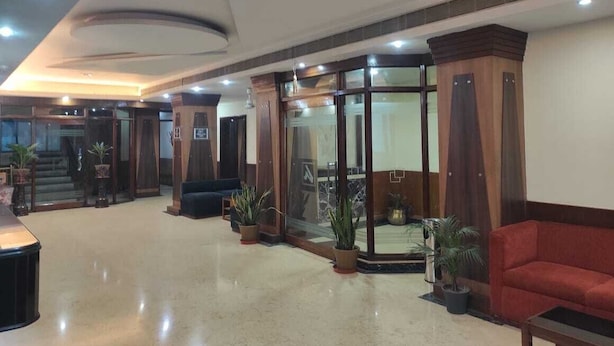 Un vestíbulo amplio con un sofá rojo, plantas en macetas y una entrada de cristal.
