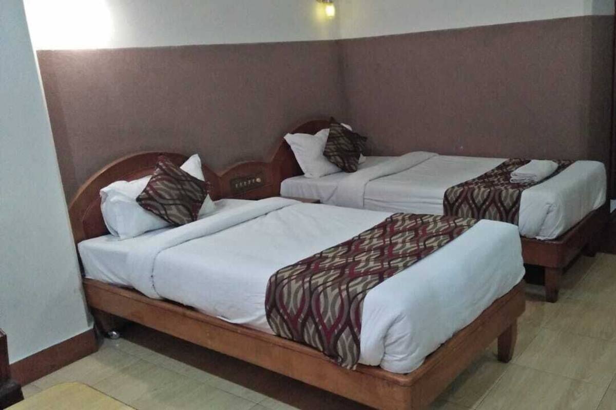 Duas camas de solteiro com estruturas de madeira e roupa de cama branca, um banco de madeira e piso de azulejos.