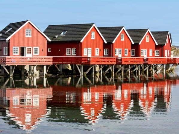 A row of red wooden houses with white trim, each with a gabled roof, situated on stilts over water.