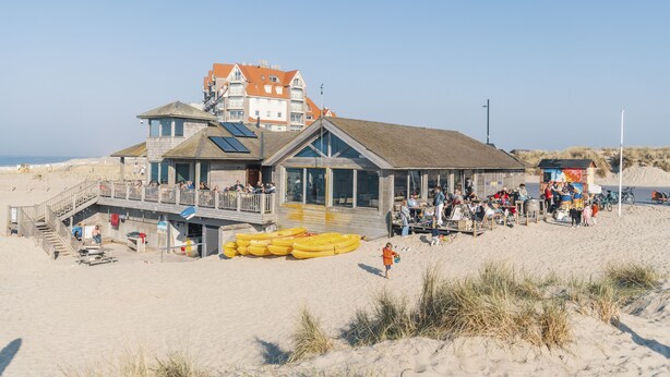 Een gebouw aan het strand met een houten terras, een uitkijktoren voor de strandwacht en een post voor de strandwacht.