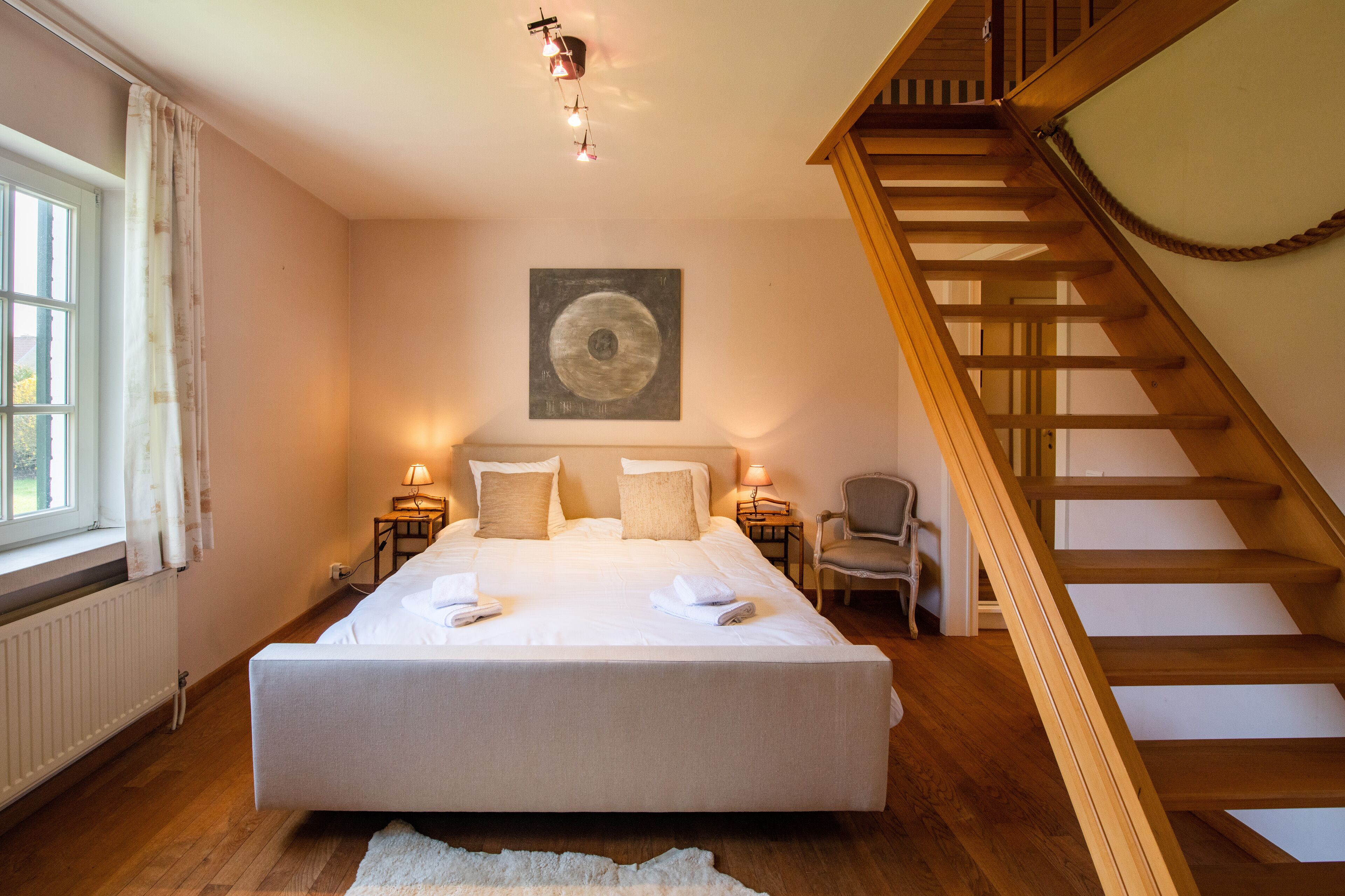 Een slaapkamer met een groot bed, een houten trap, een stoel en een schilderij aan de muur.