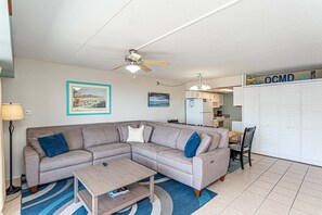 A living room with a sectional sofa, a coffee table, a ceiling fan, and a dining area with a table and chairs.
