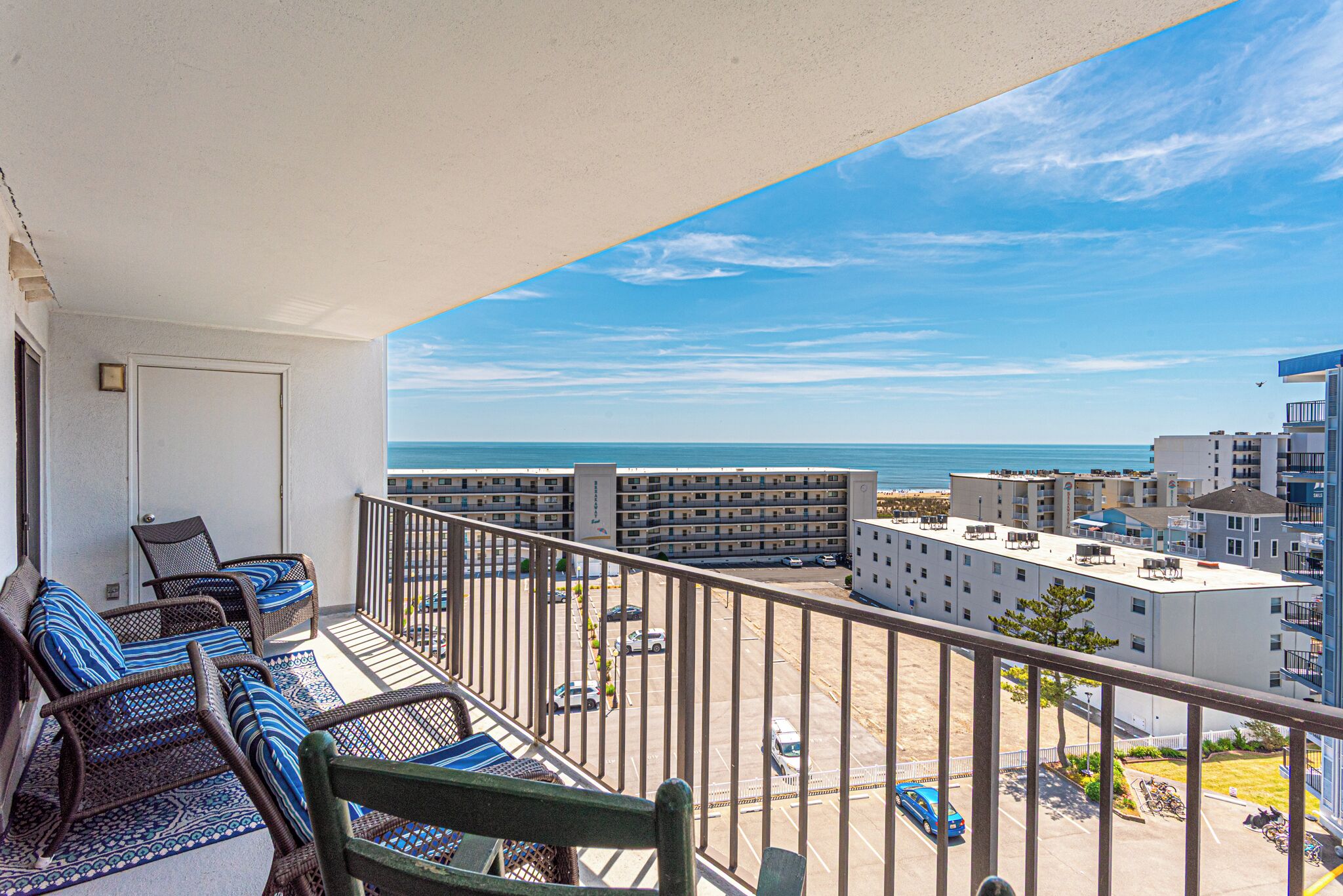 A balcony with wicker furniture, a view of the ocean, and a parking area.