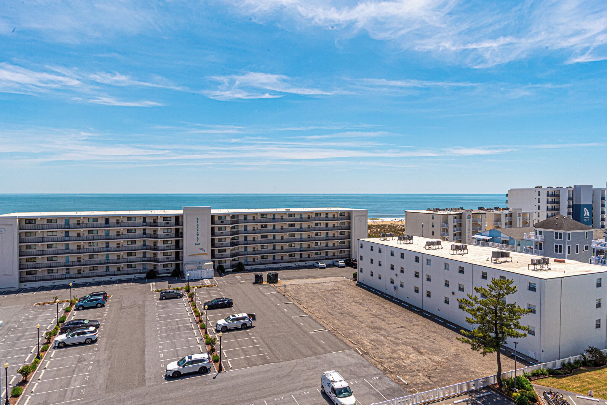 A multi-story hotel with a parking lot, a beach view, and a clear sky.