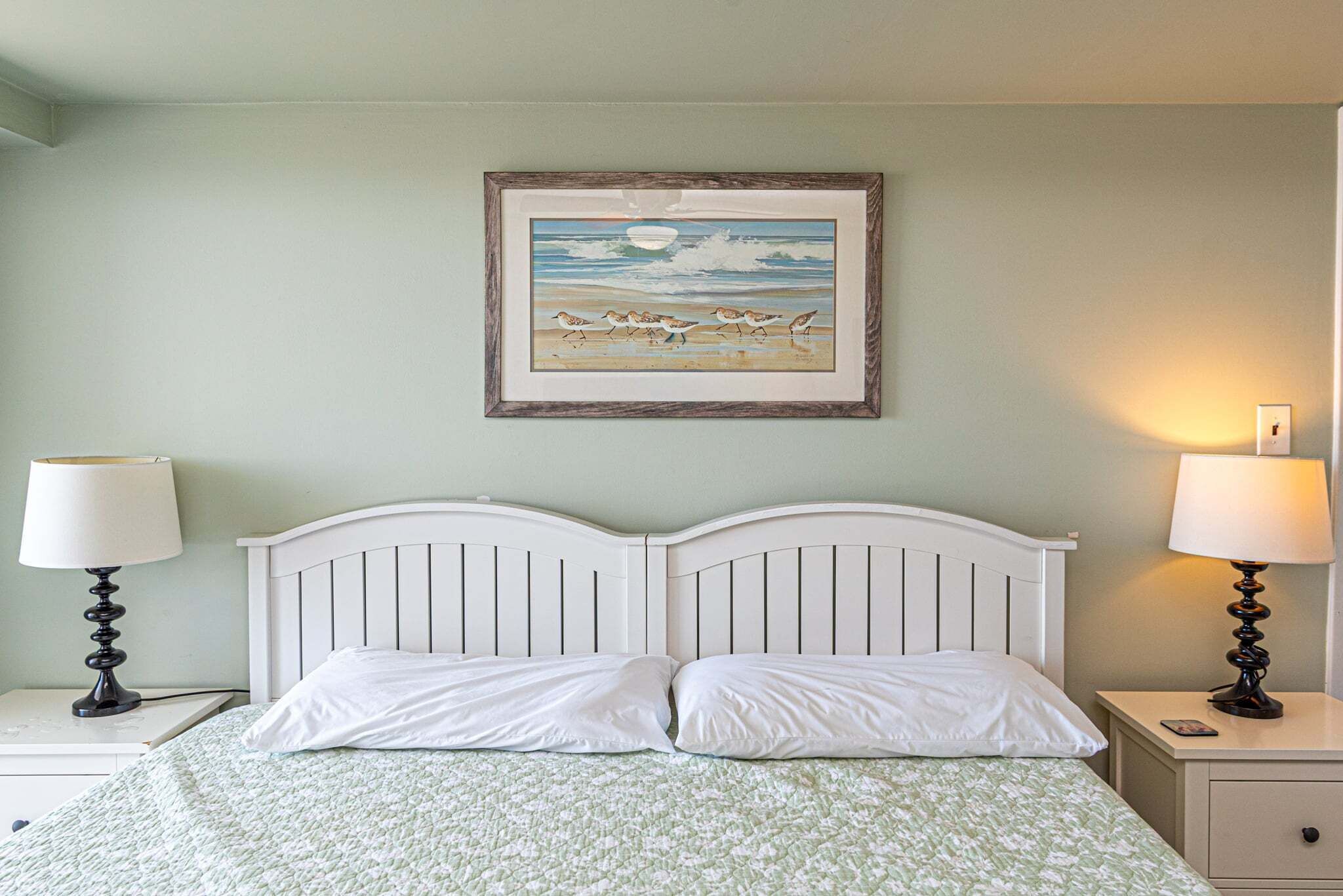 Una cama con ropa de cama blanca, cabecera, dos mesitas de noche con lámparas y un cuadro con pájaros en la pared.