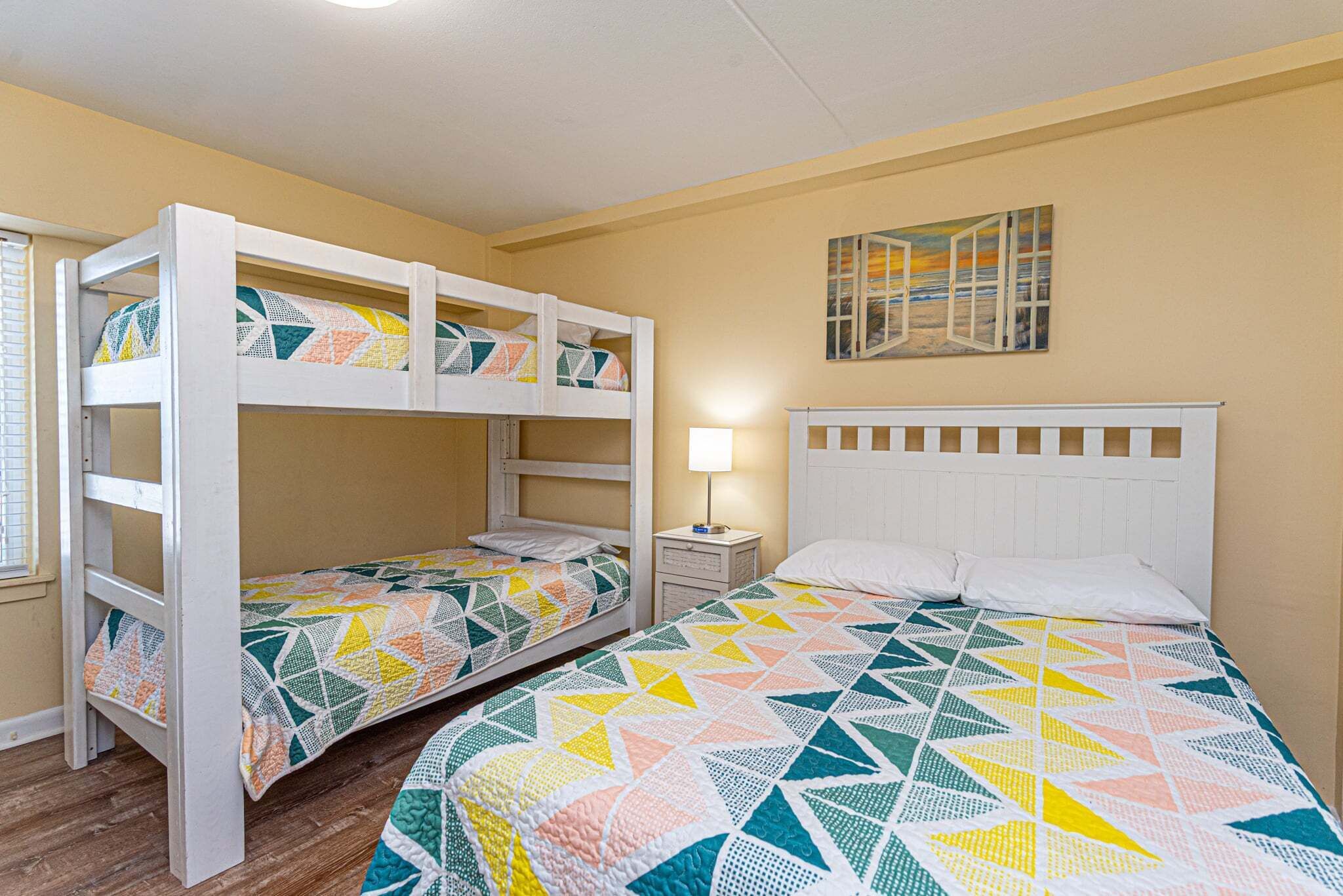 A room with bunk beds, a single bed, a nightstand, and a wall painting.