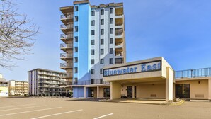 A hotel named Bluewater East with a modern design, featuring a prominent blue and beige facade, multiple balconies, and a parking lot in front. - Bluewater -3 Bedroom Condo with Outdoor Pool! (Ocean City)