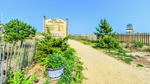 A dirt path leading to a wooden fence with a large sign indicating '135th St. June Crossing' and a city code. - Bluewater -3 Bedroom Condo with Outdoor Pool! (Ocean City)