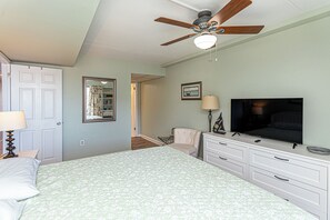 A bedroom with a bed, a ceiling fan, a television, a dresser, and a chair.