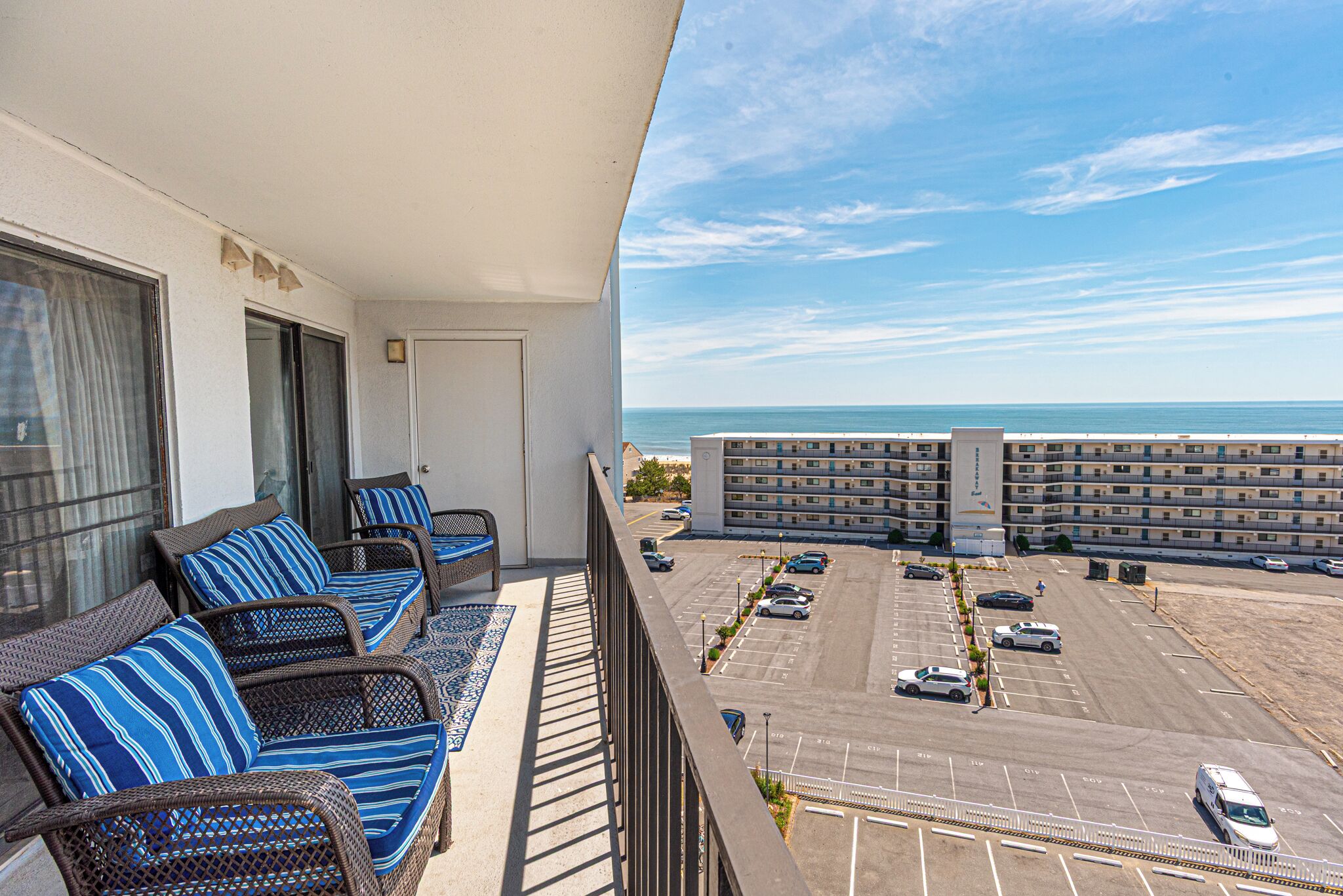 A balcony with wicker furniture and a view of a parking lot and ocean.