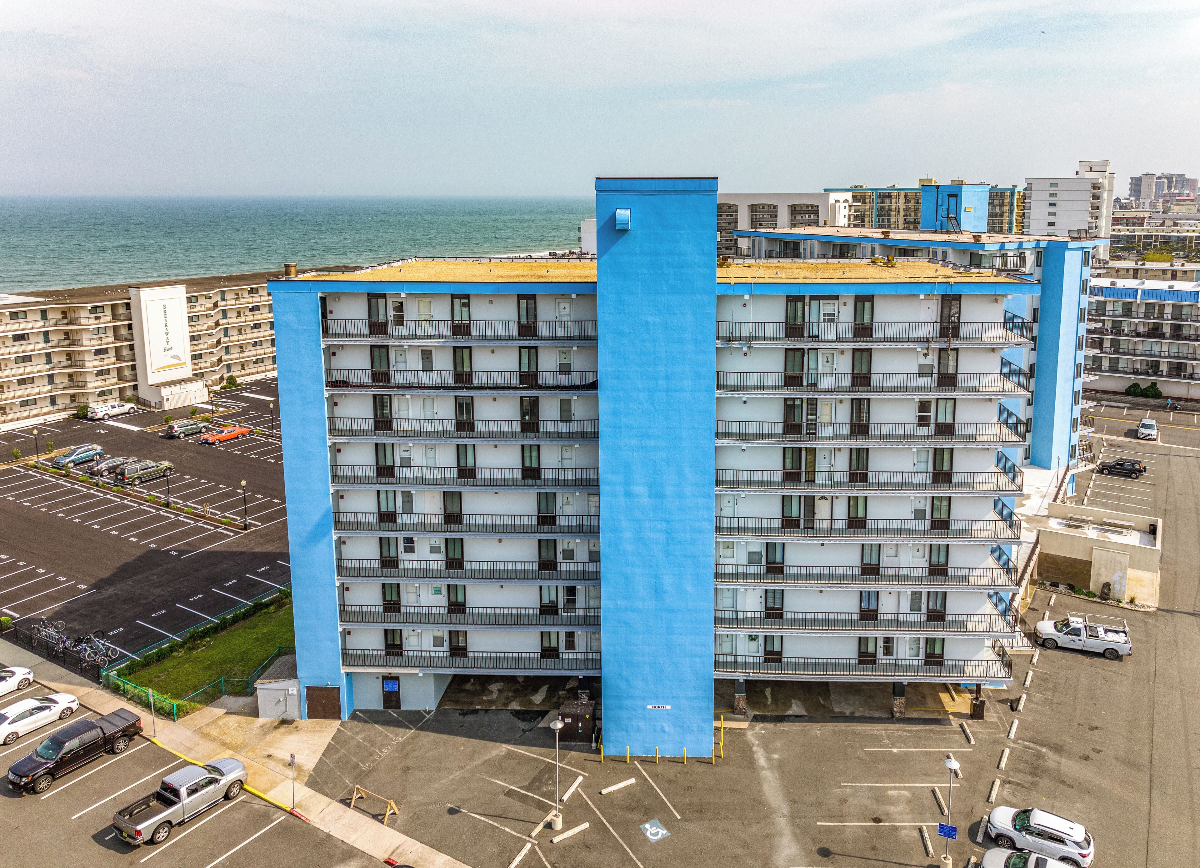 Ein Hochhaus-Hotel mit mehreren Balkonen, einem Parkplatz und Blick aufs Meer.
