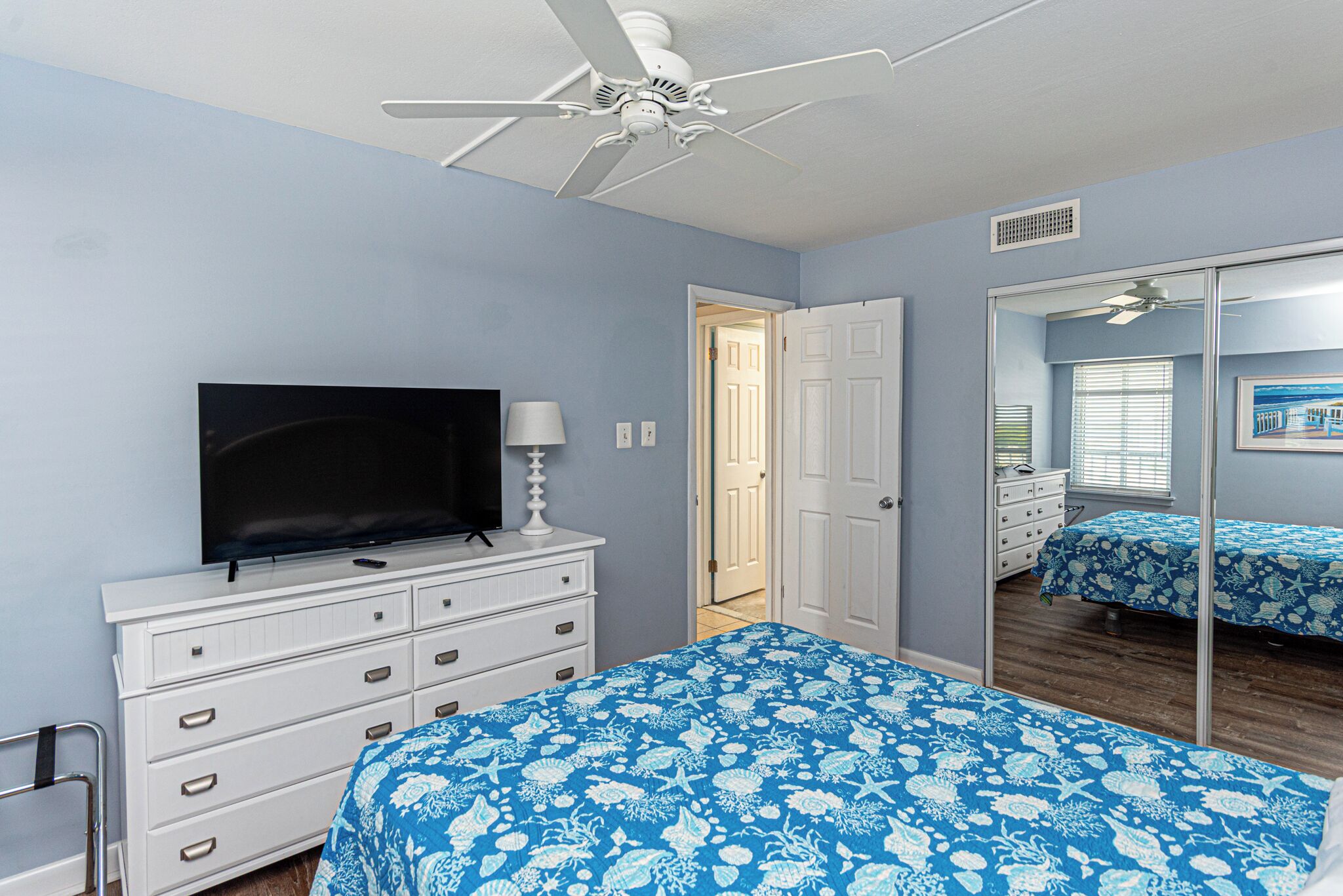 A bedroom with a bed, a dresser, a television, a ceiling fan, and a mirror.