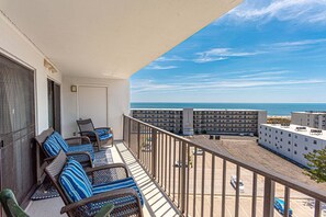 A balcony with wicker furniture, a view of the ocean, and a parking lot.