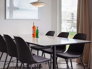 Un espace repas moderne avec une table blanche, des chaises noires et deux bouteilles posées sur la table.