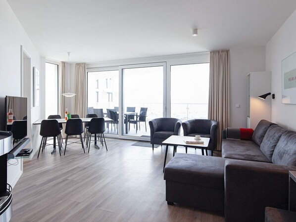 A modern living room with a sofa, chairs, a dining table, and a TV.