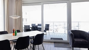 A modern room with a dining table, chairs, a sofa, and a view through large windows.
