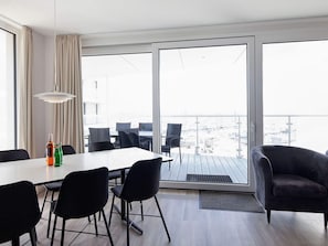 Une pièce moderne comprenant une table à manger, des chaises, un canapé et offrant une vue sur l’extérieur grâce à de grandes fenêtres.