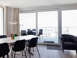 Et moderne værelse med spisebord, stole, sofa og udsigt gennem store vinduer.