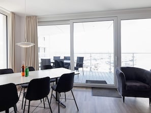 A modern room with a dining table, chairs, a sofa, and a view through large windows.