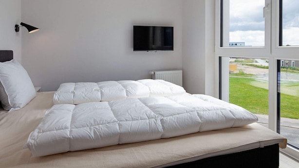A bedroom with a large bed, a mounted TV, and a view of a green landscape through the window.