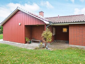 A red barn-style building with a tiled roof, a small porch, and a potted plant. - 6 Person Holiday Home in Dannemare (Dannemare)