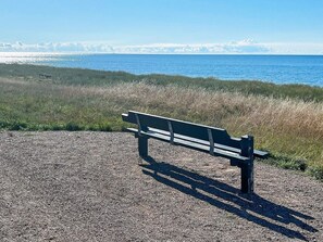 Eine Bank an einem Schotterweg mit Blick auf das Meer und ferne Berge.
