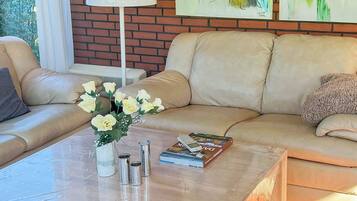 Ein Wohnzimmer mit einer Couch, einem Couchtisch mit Blumenvase, einer Lampe und einem Buch.