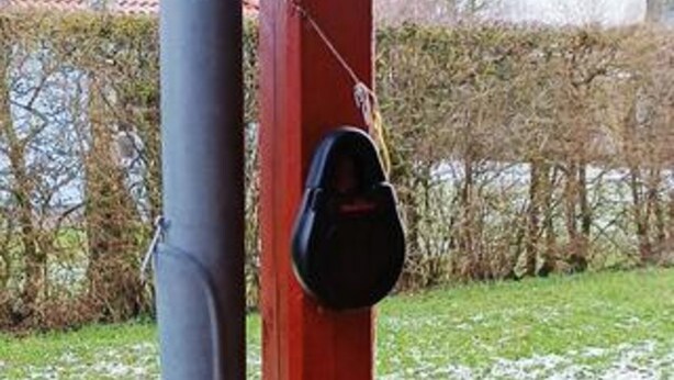 A red pole with a black object attached to it, a grey pipe, and a hedge in the background. - 6 Person Holiday Home in Dannemare (Dannemare)