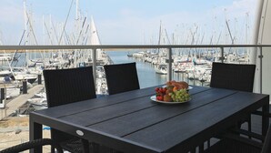 Un balcon avec une table dressée pour deux personnes, donnant sur une marina où sont amarrés de nombreux bateaux.