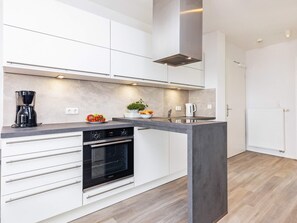 A modern kitchen with white cabinetry, a built-in oven, a coffee maker, and a fruit bowl.