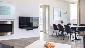 Un salon moderne doté d’un téléviseur à écran plat, d’une cheminée, d’un coin repas avec une table et des chaises, et offrant une vue sur l’extérieur.
