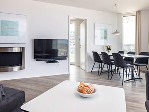 A modern living room with a flat-screen TV, a fireplace, a dining area with a table and chairs, and a view of the outdoors.