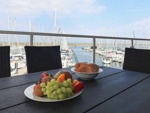 Une table avec une assiette de fruits et un panier de pain, donnant sur une marina remplie de bateaux.