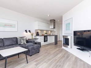 A modern living room with a grey sofa, a white coffee table, and a flat-screen TV on a white stand.