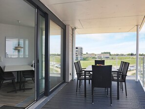 Uma varanda com mesa e cadeiras, vista de um edifício e área gramada.