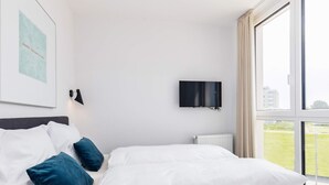 Une chambre d’hôtel avec un lit, une télévision et une fenêtre donnant sur un espace verdoyant.
