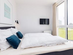 A hotel room with a bed, a television, and a window with a view of a grassy area.