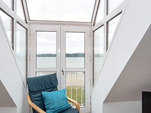 A room with a skylight, a chair with a cushion, and a view of a body of water.