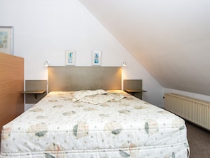 A bedroom with a bed, two bedside tables, a headboard, and a radiator.